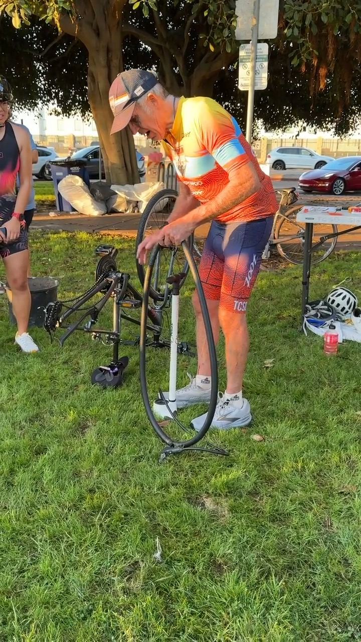 A club member in TCSD kit showing how to change a bike tire on the grass