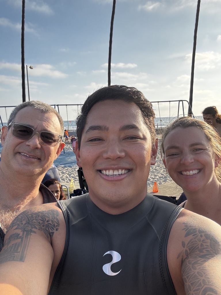 Josh in a wetsuit with two club members at the beach before a swim
