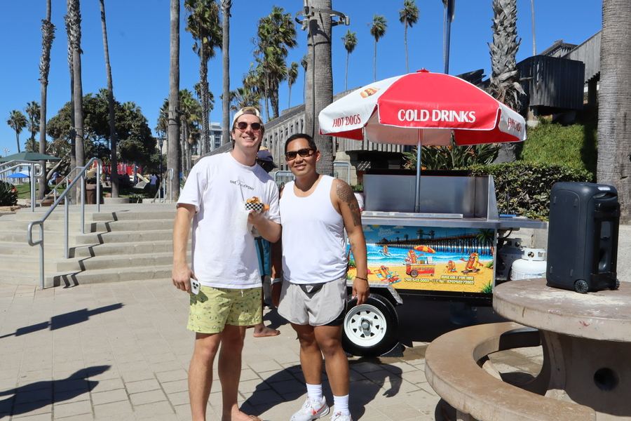 Josh and a friend with hot dogs next to the hot dog cart