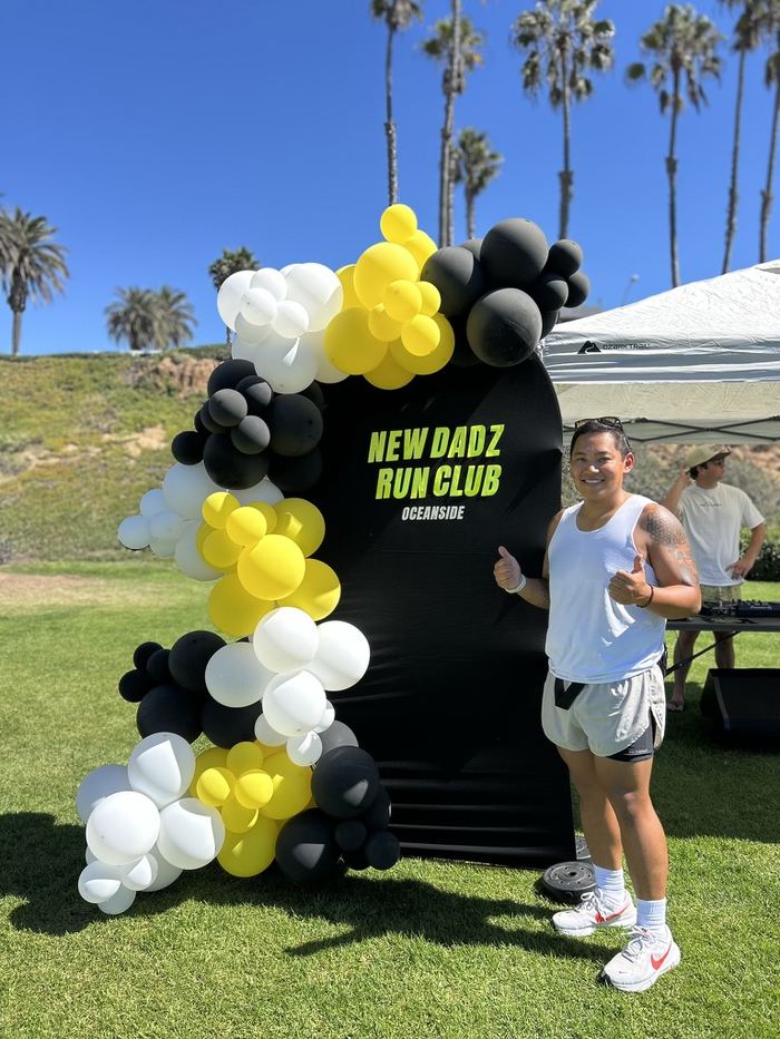 Josh giving a thumbs up next to the New Dadz Run Club backdrop