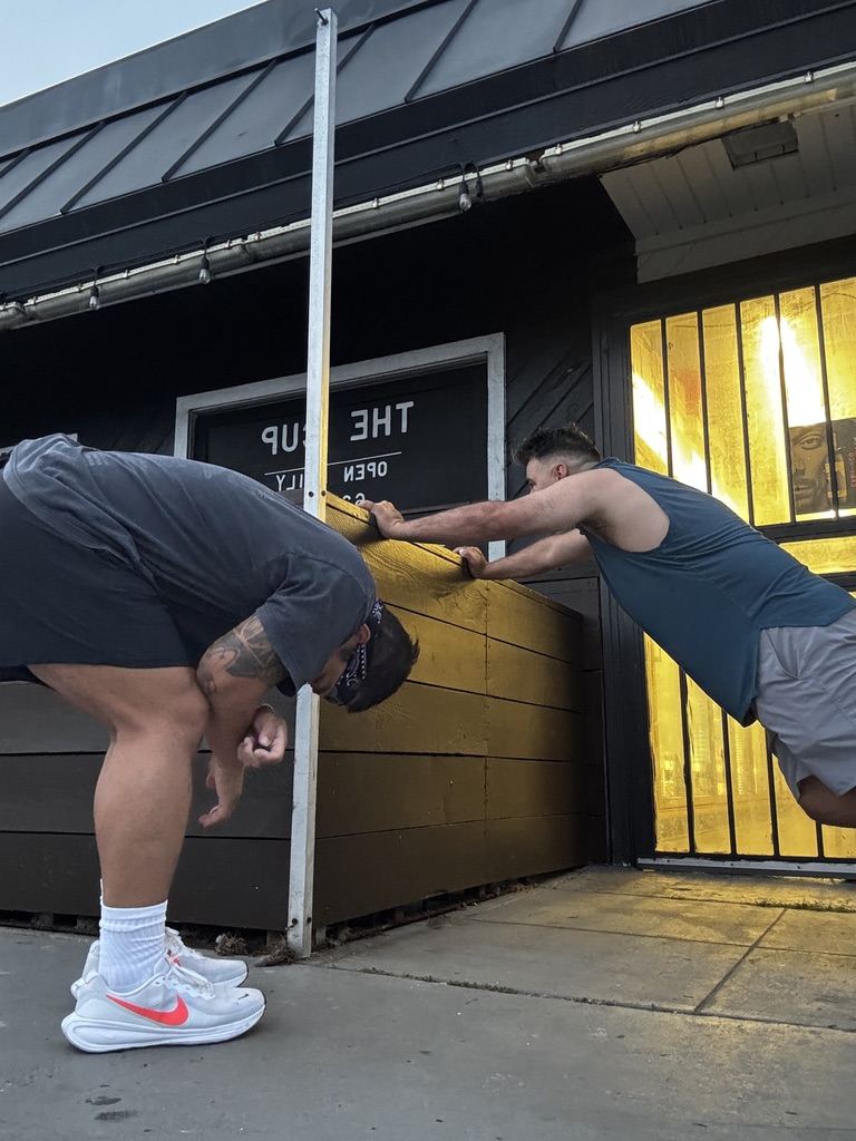 Two run club dads stretching against the planter outside The Cup after the run
