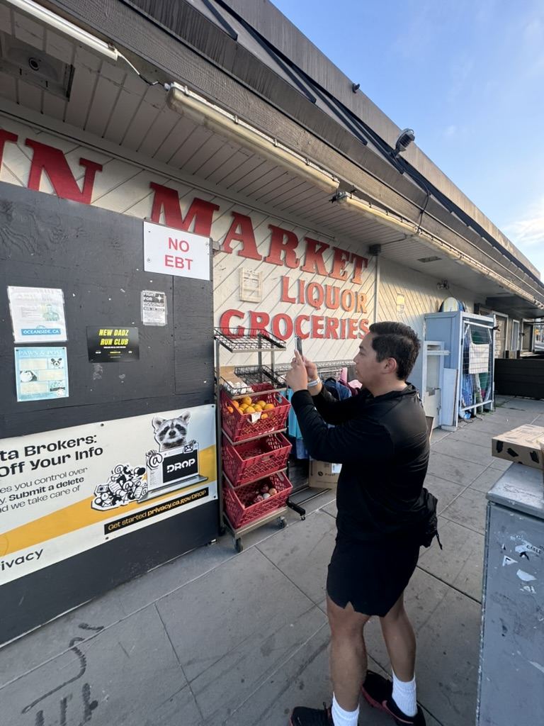 Josh photographing a New Dadz Run Club flyer posted on a market wall in Oceanside