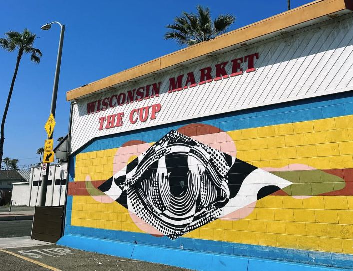 The Cup coffee shop in Oceanside, with its painted sign and a large eye mural on a yellow and blue wall