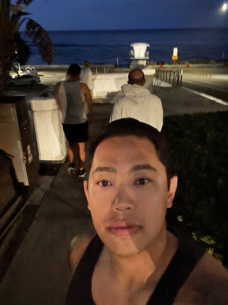 Josh taking a selfie at dawn as two run club dads head toward The Strand, the ocean and a lifeguard tower behind them